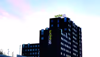 En modern hotellbyggnad i flera våningar med svart och vit fasad, med namnet "Wakeup" i ljusa gula och vita bokstäver överst. Byggnadens exteriör har flera fönster, mot en klar himmel.