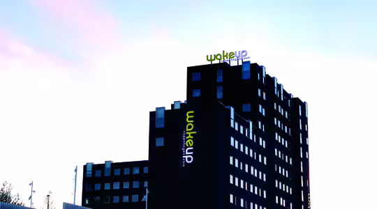 En modern hotellbyggnad i flera våningar med svart och vit fasad, med namnet "Wakeup" i ljusa gula och vita bokstäver överst. Byggnadens exteriör har flera fönster, mot en klar himmel.