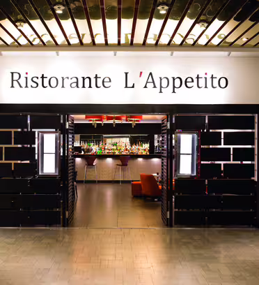 Entré till Ristorante L'Appetito, med elegant svart och brun inredning och utsikt över det väl upplysta barområdet inuti. Restaurangens namn visas tydligt ovanför dörröppningen.