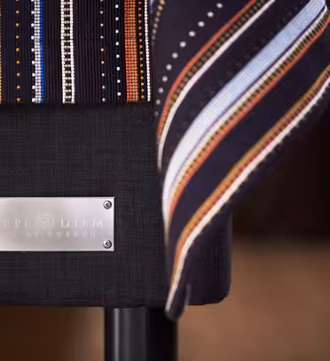 Närbild av en svart bänk med en metalletikett med texten "Carpe Diem, Made in Sweden." Ett färgglatt randigt tyg draperar över bänkkanten. Bakgrunden är suddig, vilket framhäver texturerna och mönstren på tyget och etiketten.