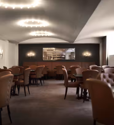 Elegant restauranginteriör med mjuk belysning, med bruna läderstolar runt mörka träbord. En dekorativ spegel och dämpade vägglampetter pryder väggarna och skapar en inbjudande och sofistikerad atmosfär.