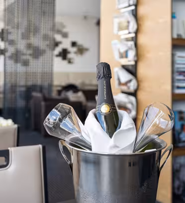 Champagneflaska i en ishink med glas, som ställs på ett restaurangbord. Bakgrunden visar böcker på hyllor, modern inredning och matstolar, vilket skapar en elegant atmosfär.