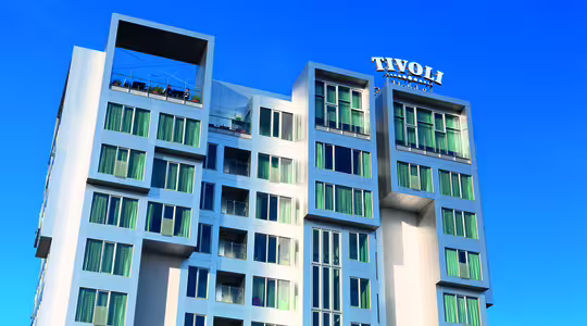 En modern hotellbyggnad i flera våningar med en elegant design mot en klarblå himmel. Strukturen har många fönster och en takterrass. Hotellets namn och logotyp visas tydligt högst upp.
