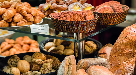 En visning av olika bakverk, inklusive korgar med croissanter, bakverk och skivat bröd. Det finns också olika frallor och bröd, som baguetter och rustikt bröd, på svarta och vävda korgar. En skylt märkt "croissanter" är synlig.